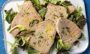 Fette di tonno al forno, dorate e succulente, servite su un letto di insalata fresca con scorza di limone e erbe aromatiche.