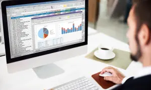 Mężczyzna pracuje przy komputerze, analizując dane w arkuszu kalkulacyjnym, przypominającym ten z programu **jeżeli excel**. Na ekranie widoczne są wykresy i tabele.