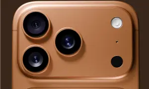 Gros plan sur le module caméra d'un iPhone couleur or. Trois objectifs noirs et un flash blanc sur un fond brun.