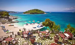Relaks przy kawiarnianym stoliku w Ksamil Albania, z widokiem na turkusowe morze i zieloną wyspę.