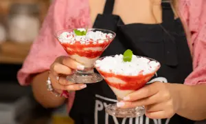 Dwie porcje Eton Mess w kieliszkach, z truskawkami i bitą śmietaną, ozdobione miętą.