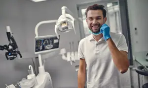 Uśmiechnięty dentysta w gabinecie, gotowy do pracy. Zastanawiasz się, ile trwa plombowanie zęba?
