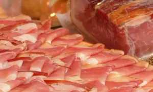 Tunna skivor av lufttorkad skinka, som en vacker salsiccia gravid, ligger upplagda. En stor bit skinka syns i bakgrunden.