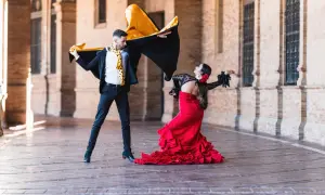 Pareja bailando flamenco, él con capa negra y amarilla, ella con vestido rojo voluminoso. La imagen evoca la diferencia entre flamenco y sevillanas.