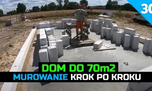 Budowa domu 70m2: murowanie ścian z bloczków betonowych. W tle plac budowy i pracownik.