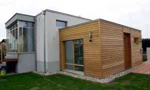 Moderner Anbau an altes Haus: Ein Teil des Hauses ist mit Holz verkleidet, der andere Teil verputzt. Große Fensterfronten und ein Wintergarten.