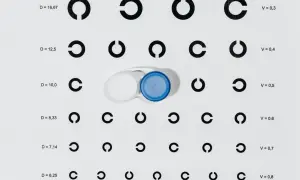 Tabela optometryczna z cyframi i otwartymi okręgami, obok pojemnik na soczewki kontaktowe.