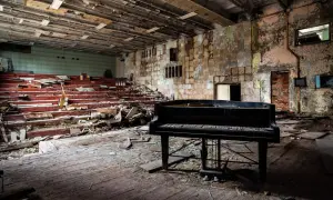 Un piano noir trône au milieu d'une salle délabrée, vestiges de maisons abandonnées. Les sièges rouges sont brisés, le sol jonché de débris.
