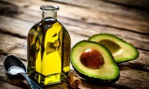 Botella de aceite de aguacate para la piel, junto a un aguacate cortado y una cuchara con aceite.