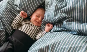 En 5 månaders bebis sover sött i ett randigt täcke. Kanske drömmer hen om att slippa vakna ofta på natten.