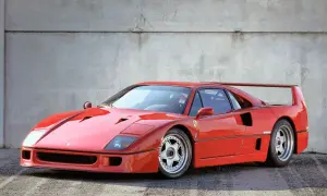 Ikoniczny czerwony Ferrari F40 z charakterystycznym skrzydłem, zaparkowany na tle betonowej ściany.