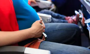 Gravid kvinna med magen i fokus, bekvämt sittande på ett flygplan. Hon håller handen över magen, redo att flyga gravid.