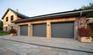Tre moderna garageportar i mörkgrått framför ett hus med träfasad och tegelfasad.