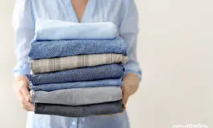 Ein Stapel frisch gewaschener Hemden in verschiedenen Blautönen und Mustern, gehalten von einer Person in einem hellblauen Hemd.