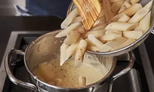 Schwarzwurzeln werden für ein leckeres Rezept in eine cremige Sauce gegeben. Ein Holzlöffel hilft beim Einfüllen.