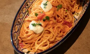 Un invitante piatto di pasta con pomodorini, condita con una cremosa salsa e guarnita con ricotta fresca e basilico.