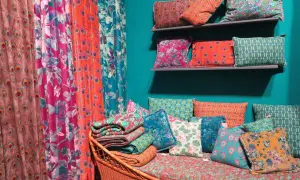 Rideau **couleur corail** et coussins aux motifs floraux et paons, sur un banc en rotin.