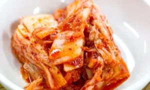 Domowe kimchi w białej miseczce, z widocznymi liśćmi kapusty i czerwoną przyprawą.