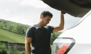 Mężczyzna zmartwiony przy otwartym bagażniku samochodu. W razie awarii pomoże ubezpieczenie assistance.