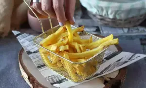 Złociste frytki w metalowym koszyku, ręka sięga po jedną.