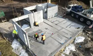 Budowa domu z keramzytu. Widać elementy konstrukcyjne, pracowników i dźwig. Śnieg na placu budowy może sugerować wady związane z warunkami atmosferycznymi.