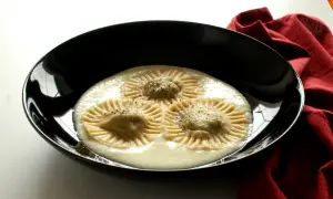 Tre ravioli di borragine, con un ripieno cremoso e una spolverata di pepe, serviti in una ciotola nera su un tovagliolo rosso.