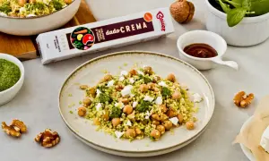 Piatto di cous cous con ceci, formaggio e pesto. Un'idea gustosa per un pasto veloce e saporito.