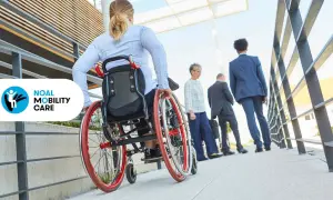 Donna in sedia a rotelle sale una rampa con lieve pendenza, seguita da altre persone.