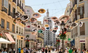 Ojos flotantes decoran una calle famosa de Málaga, observando a la multitud que pasea entre edificios históricos.
