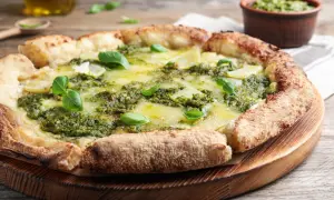 Pizza rustique au pesto, garnie de fines tranches de pommes de terre et de fromage fondant, décorée de feuilles de basilic frais.