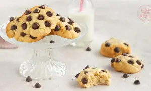 Saftige low carb Kekse mit Schokostückchen auf einem Glasständer, daneben ein Glas Milch und weitere Kekse.