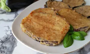 Fette dorate di cordon bleu di melanzane, impanate e fritte, servite su un piatto bianco con foglie di basilico fresco.