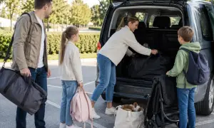 Familjen packar sin caddy hybrid inför resan. Pappa bär en stor väska, medan barnen har ryggsäckar. Mamma lägger in mer bagage i bilen.