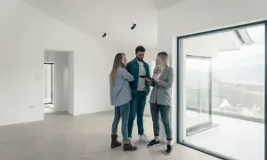 Para odbiór techniczny mieszkania na co zwracać uwagę? Para ogląda tablet z agentką nieruchomości w nowym, jasnym mieszkaniu z widokiem.