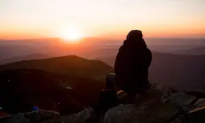 Sonnenuntergang in den Hohen Tatra. Eine Person sitzt auf einem Felsen und blickt auf die Berge.