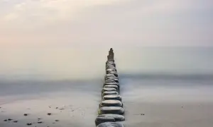 Linia drewnianych pali na plaży, prowadząca w spokojne morze, tworzy stan zen.