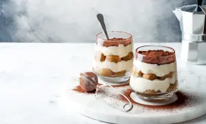 Dwa pucharki z kremowym, warstwowym deserem, posypane kakao. To najprostsze tiramisu, idealne na deser.