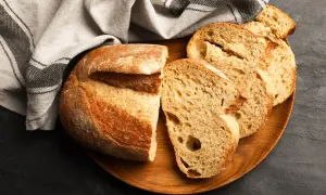 Świeży chleb pokrojony na desce, obok lniana ściereczka. Dowiedz się, jak przechowywać chleb, by był zawsze pyszny.
