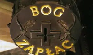 Napis "Bóg zapłać" na okrągłej tablicy z krzyżem i liśćmi. Może to być związane z funduszem kościelnym.