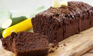 Saftiger Schokoladen-Zucchini-Kuchen mit Schokoladenglasur und zwei Herz-Dekorationen, daneben liegen frische Zucchini.
