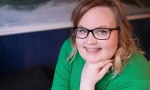 Kvinna med glasögon och grön tröja ler, trots morgonens ångest och depression.
