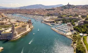 Widok na port w Marsylii, z fortecą i licznymi jachtami. W tle widać miasto i góry. Podróż z Nicei do Marsylii to wspaniała przygoda.