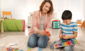 Psycholog dziecięcy i chłopiec bawią się klockami i cymbałkami na dywanie.