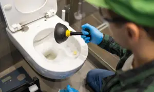 Persona con guanti blu usa uno stantuffo per smontare wc otturato.