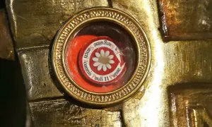 Złota oprawa zawiera relikwie, okrągły medalik z napisem "Ex Sanguine Sancti Joannis Pauli II Papae" i białym kwiatkiem.