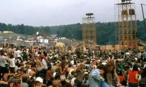 Tłum ludzi na festiwalu, gdzie jest Woodstock? Widać scenę, wieże głośnikowe i namioty.