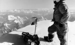 Bergsteiger auf dem Gipfel des K2, der die Erstbesteigung feiert. Ausrüstung und Fahne im Schnee.