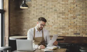 Mężczyzna w fartuchu analizuje dokumenty, obok laptop i notatnik. Może sprawdzać swój iban pko.