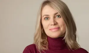 Kobieta po 50-tce z niebieskimi oczami i blond włosami, zastanawiająca się nad zabiegami na twarz.
