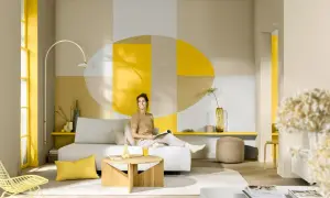 Frau entspannt auf Sofa in modernem Wohnzimmer. Die Wandgestaltung mit Gelb und Grau zeigt, welche farbe passt zu gelb.